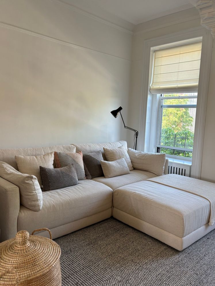 Beige sectional couch in a living room with several throw pillows on it.
